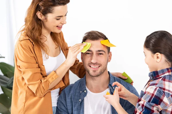 Glückliche Frau und Kind legen gelbe Klebezettel auf fröhlichen Mann — Stockfoto