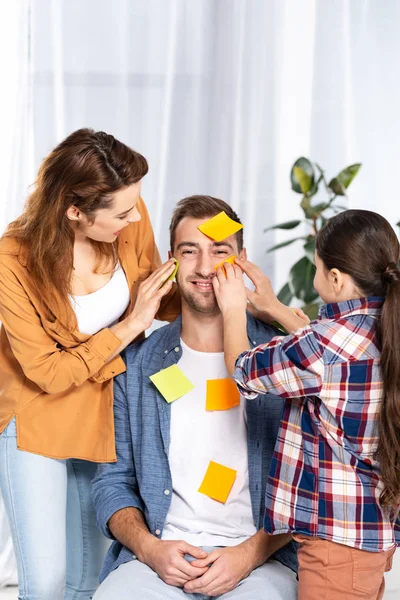 Cheerful woman and kid putting yellow sticky notes on handsome man — Stock Photo