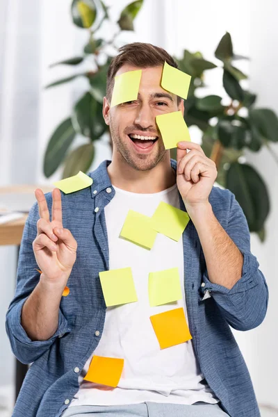 Hombre feliz en amarillo y naranja notas adhesivas que muestran signo de paz - foto de stock