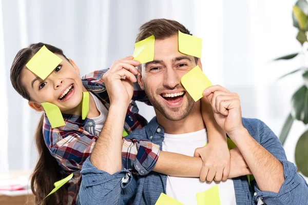 Criança alegre abraçando pai feliz em notas pegajosas amarelas — Fotografia de Stock