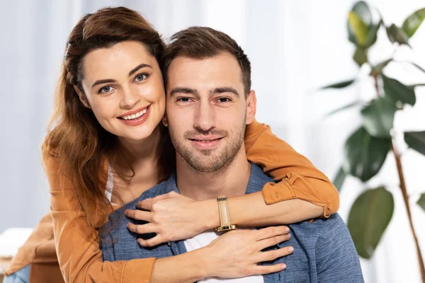 Mujer alegre abrazando al hombre feliz y sonriendo en casa - foto de stock