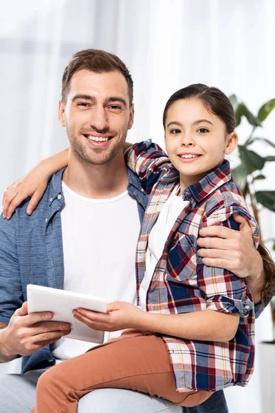 Glückliches Kind, das neben seinem schönen Vater sitzt und ein digitales Tablet in der Hand hält — Stockfoto