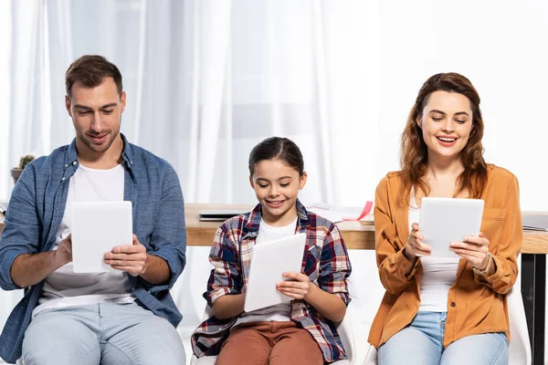 Pais alegres sentados com criança feliz e usando comprimidos digitais — Fotografia de Stock