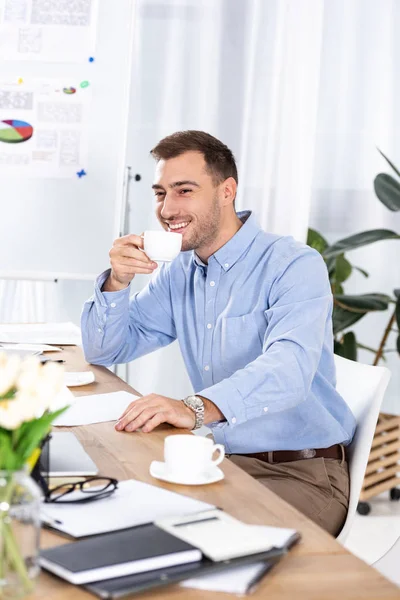 Empresário alegre segurando xícara de café enquanto sentado no escritório — Fotografia de Stock