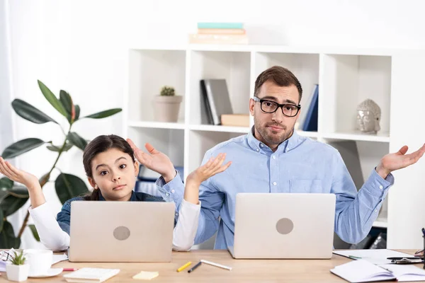 Hombre guapo en gafas y linda hija gesto cerca de computadoras portátiles - foto de stock