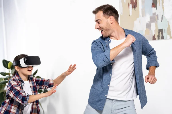 Padre feliz corriendo desde lindo niño en auriculares de realidad virtual - foto de stock