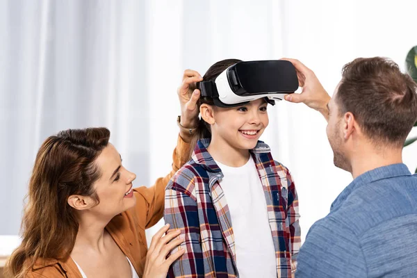 Pais alegres olhando para criança feliz em fone de ouvido realidade virtual — Fotografia de Stock