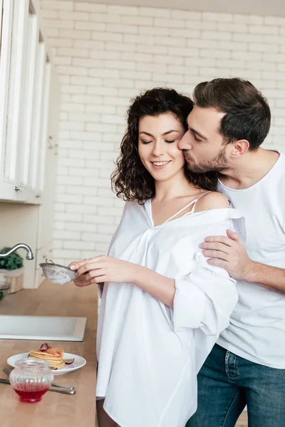 Hombre besando novia mientras ella preparando el desayuno en la cocina — Stock Photo