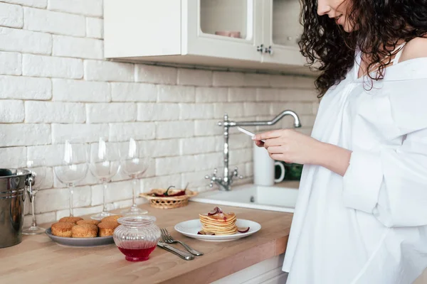 Частичный вид красивой девушки в белой рубашке с помощью смартфона на кухне — стоковое фото