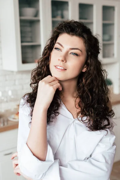 Jeune femme rêveuse avec les cheveux bouclés regardant loin dans la cuisine — Photo de stock