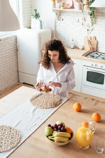 Vista aérea de la mujer bonita comiendo panqueques en la cocina - foto de stock