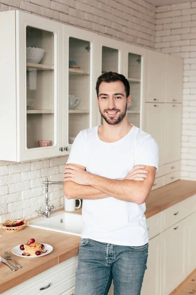 Sorrindo barbudo homem de pé com os braços cruzados na cozinha — Fotografia de Stock