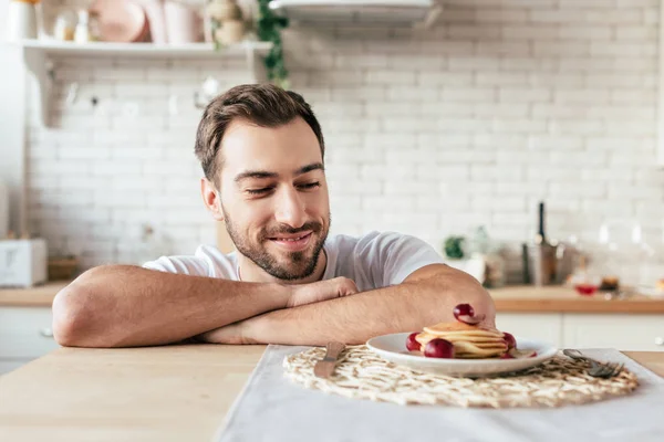 Sourire homme barbu regardant des crêpes dans la cuisine — Photo de stock