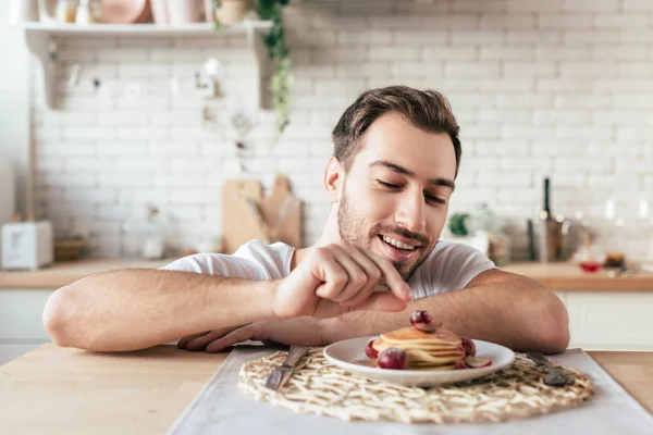 Smiling bearded man sitting at table with plate on pancakes — Stock Photo