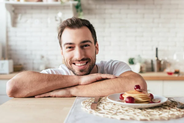 Front view of laughing man sitting at table with plate on pancakes — Stock Photo