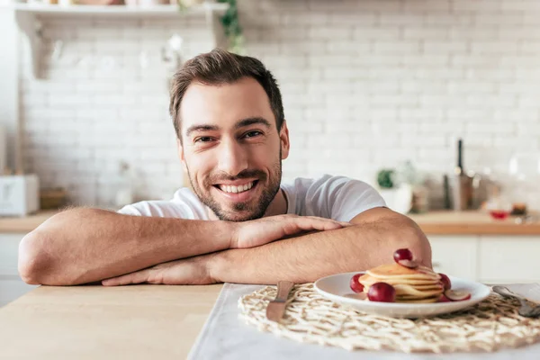 Vista frontale di uomo ridente seduto a tavola con piatto su frittelle — Foto stock