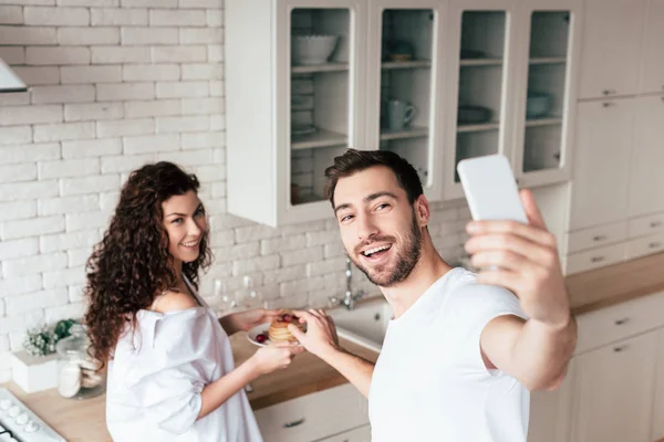 Усміхнена пара бере селфі з млинцями на кухні — стокове фото