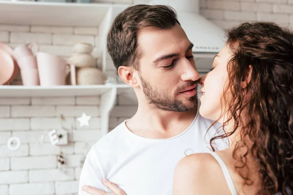 Encaracolado jovem mulher beijando namorado barbudo na cozinha — Fotografia de Stock