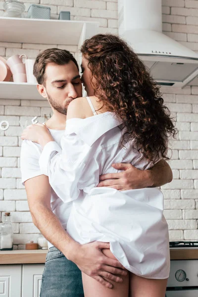 Man embracing sexy girlfriend and kissing her in shoulder in kitchen — Stock Photo