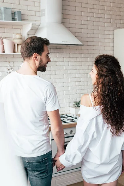 Vista trasera de la pareja tomados de la mano y mirándose en la cocina - foto de stock