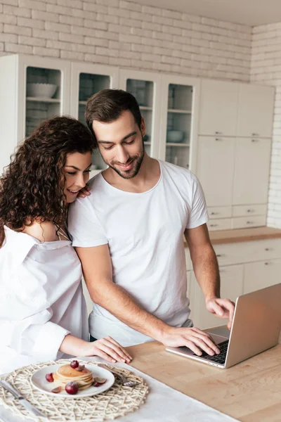 Smiling couple using laptop during breakfast in kitchen — Stock Photo