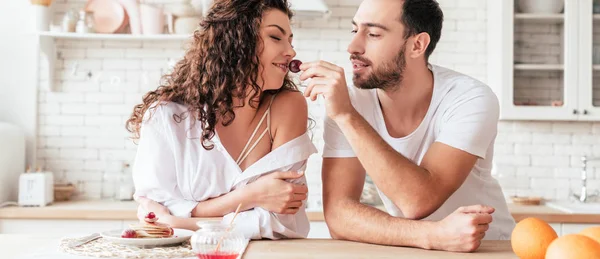 Panoramic shot of bearded man feeding girlfriend with berry — Stock Photo