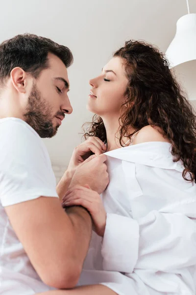 Bearded man undressing curly girlfriend with closed eyes — Stock Photo