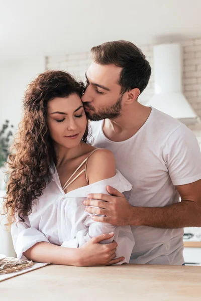 Barbudo hombre abrazando y besando novia en cocina - foto de stock