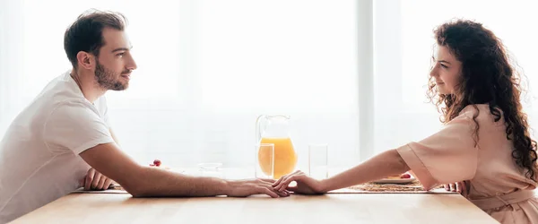 Panoramic shot of couple touching hands and looking at each other during breakfast — Stock Photo