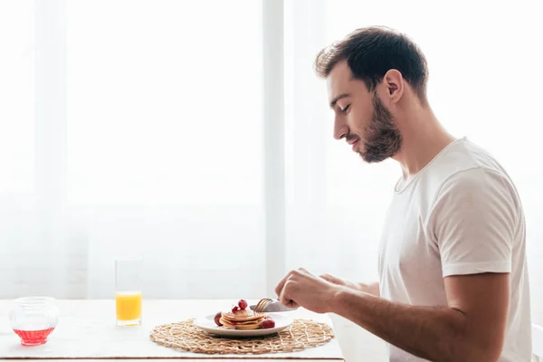 Vue latérale de l'homme barbu manger des crêpes dans la cuisine — Photo de stock