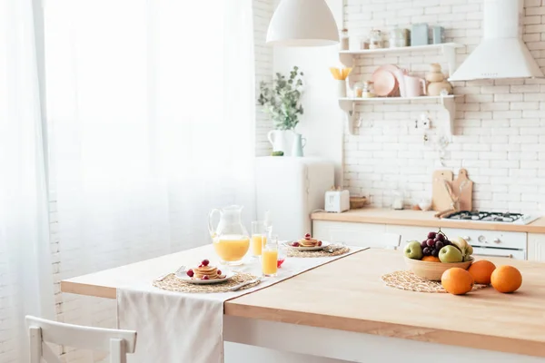 Served table with pancakes, fruits and orange juice in kitchen — Stock Photo