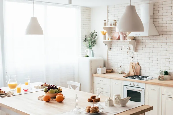 Modern kitchen with fruits, pancakes, cakes, croissants and oranje juice on table — Stock Photo