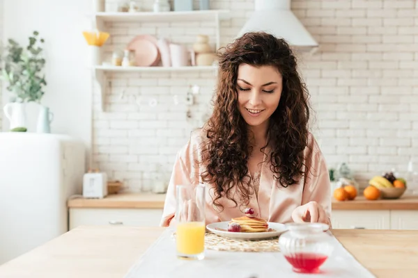 Charmantes lockiges Mädchen, das Pfannkuchen mit einem Lächeln betrachtet — Stockfoto