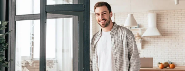 Plano panorámico de hombre barbudo sonriente en camisa a cuadros mirando a la cámara - foto de stock