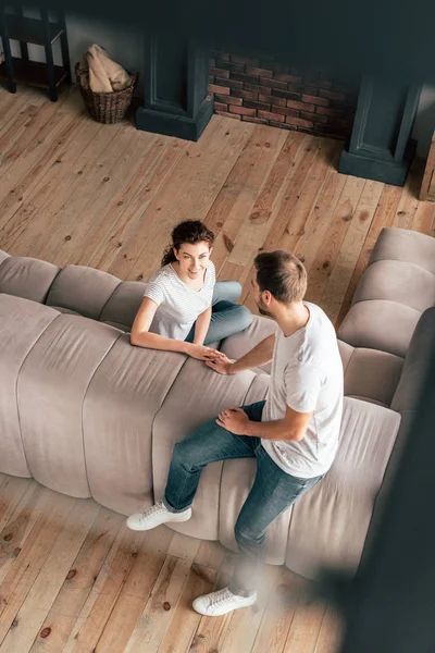 Blick von oben auf ein Paar, das auf dem Sofa sitzt und die Hände im Wohnzimmer berührt — Stockfoto