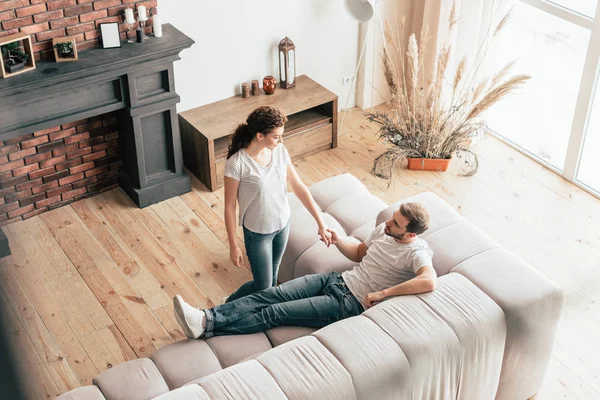 Vista aérea de feliz pareja cogida de la mano en la sala de estar - foto de stock