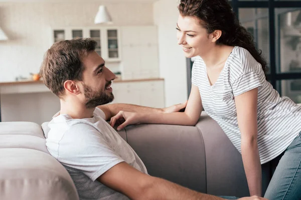 Smiling couple sitting on sofa and looking at each other — Stock Photo