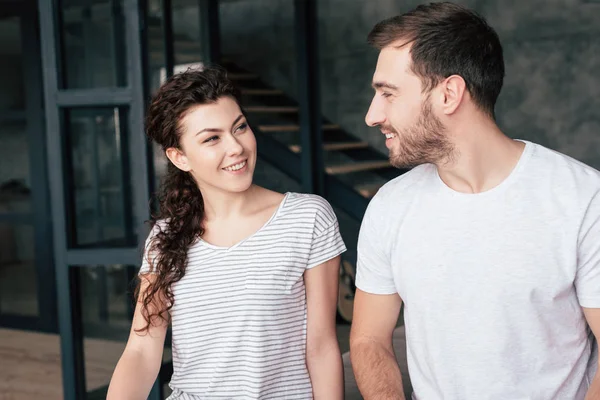 Coppia sorridente in t-shirt guardarsi a casa — Foto stock