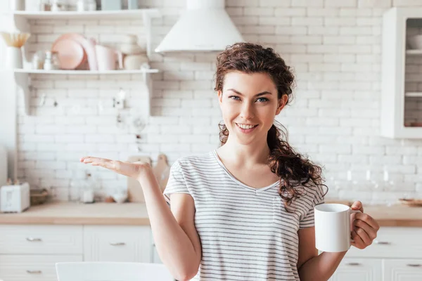 Vista frontal de chica atractiva sosteniendo taza de café en la cocina - foto de stock