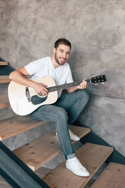 Усміхнений бородатий чоловік сидить на сходах і грає на акустичній гітарі — стокове фото