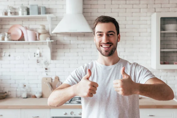 Frontansicht eines lachenden bärtigen Mannes, der in der Küche Daumen nach oben zeigt — Stockfoto