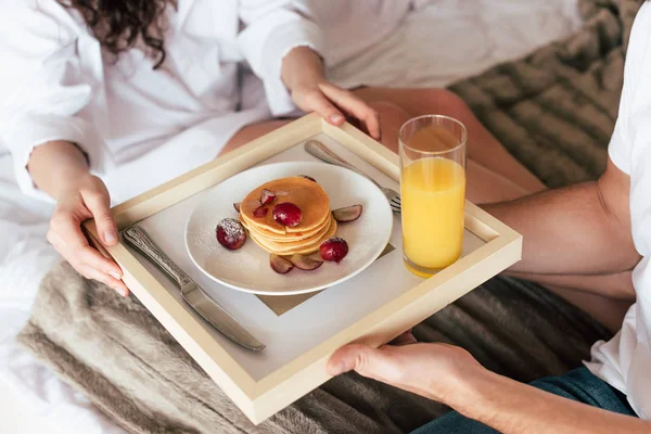 Partial view of couple holding tray with pancakes and glass of orange juice — Stock Photo