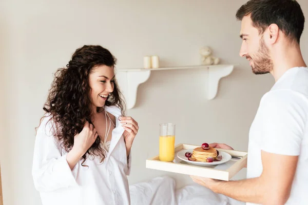 Cropped view of man holding tray with breakfast for girlfriend in bedroom — Stock Photo