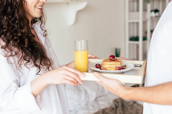 Partial view of couple holding tray with pancakes and orange juice in bedroom — Stock Photo