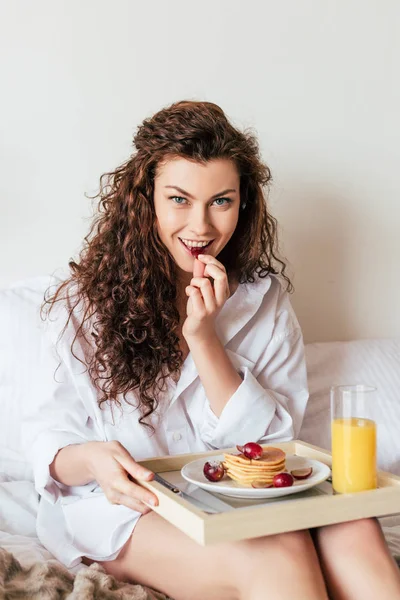 Charming sexy girl in shirt having breakfast in bed — Stock Photo