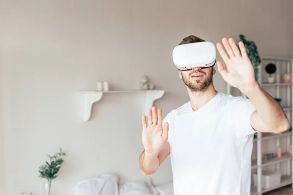 Hombre emocional en auriculares vr agitando las manos en el dormitorio - foto de stock