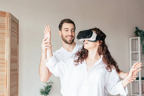 Chica sorprendida en vr auriculares cogidos de la mano con el novio en el dormitorio - foto de stock