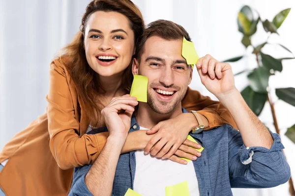 Cheerful woman hugging handsome man with yellow sticky notes — Stock Photo