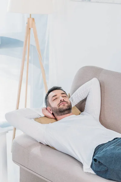 Schöner bärtiger Mann mit geschlossenen Augen und Händen auf dem Rücken, der zu Hause auf der Couch schläft — Stockfoto