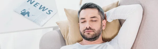Tiro panorâmico de homem barbudo bonito com os olhos fechados descansando no sofá em casa — Fotografia de Stock